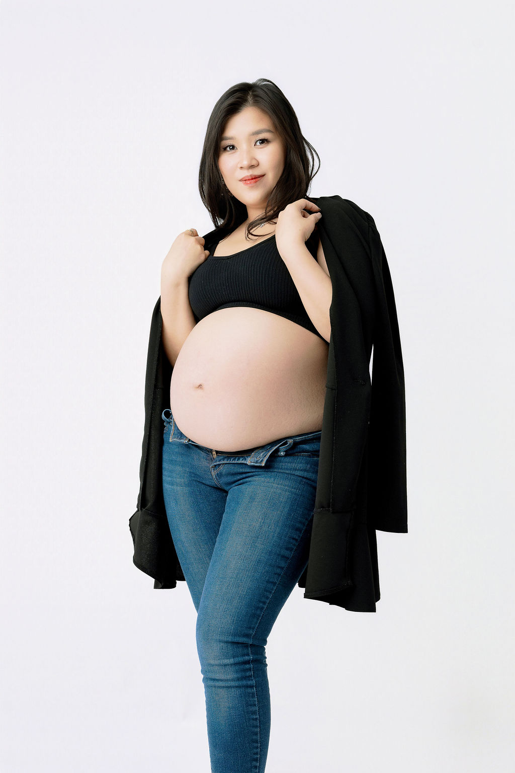 A smiling pregnant woman stands holding a black sweater on her shoulders with her bump out in jeans after a 3d ultrasound in austin