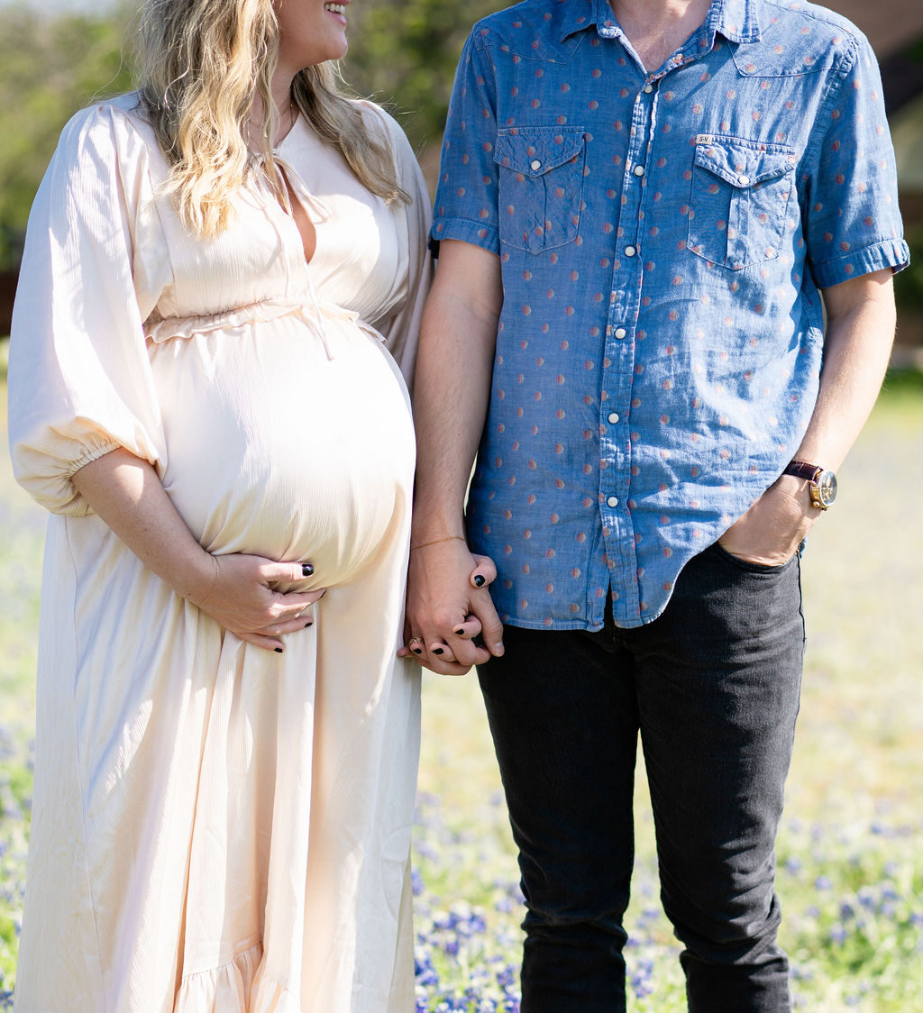 A happy couple hold hands in blue and a cream maternity gown ina. field of matching flowers after visiting birth centers in austin