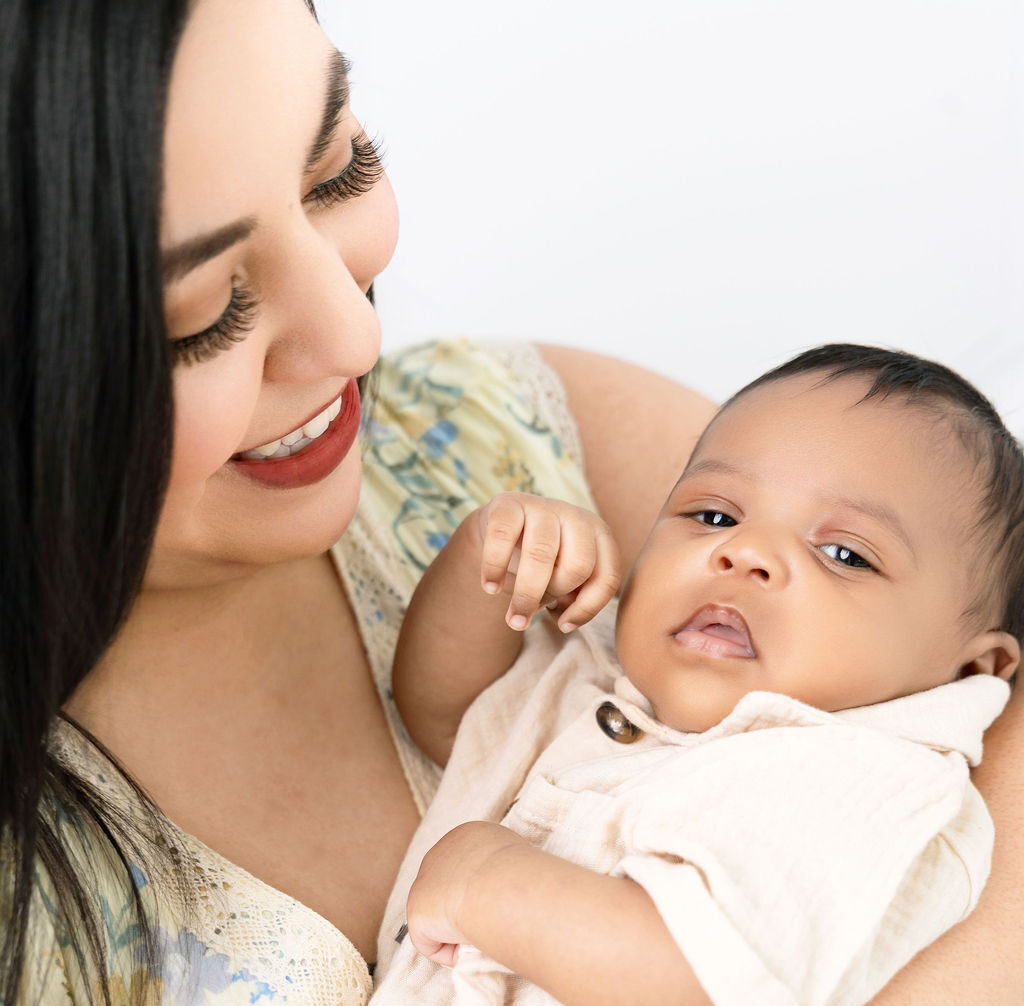 A baby boy in a tan onesie lays in mom's arms in a studio after meeting great nannies in austin