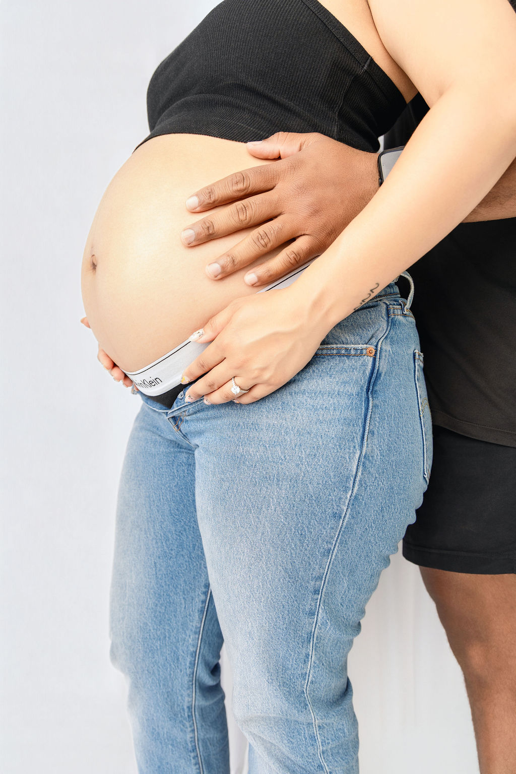 A happy pregnant couple hold the bump in jeans and black top in a studio after some prenatal yoga in austin