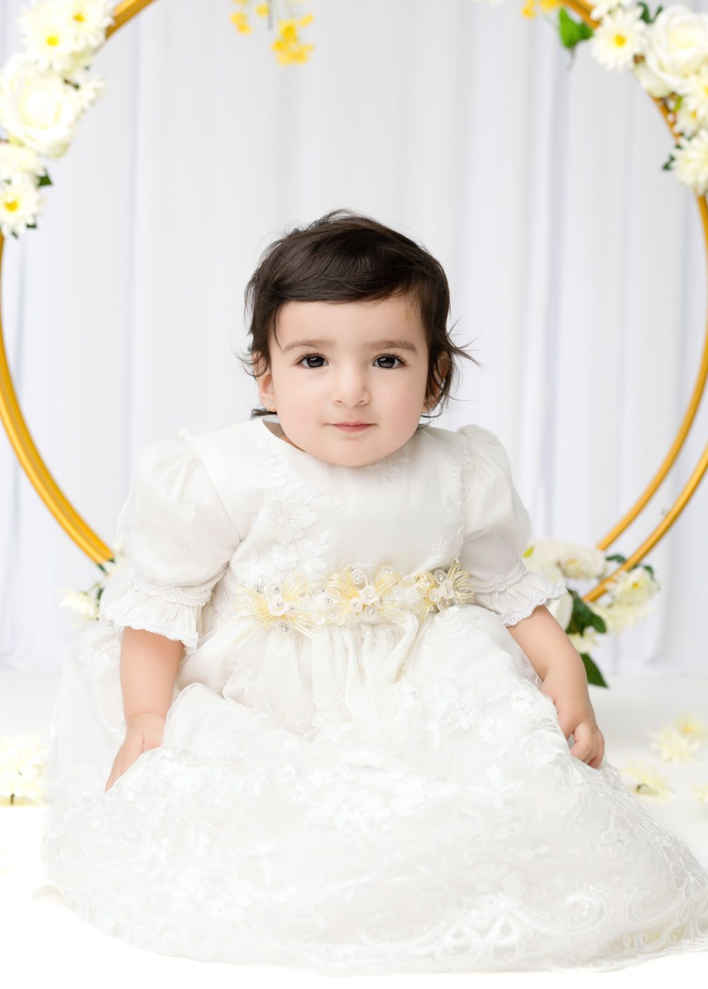 A toddler girl in a white lace dress sits in a studio smiling after visiting daycares in austin