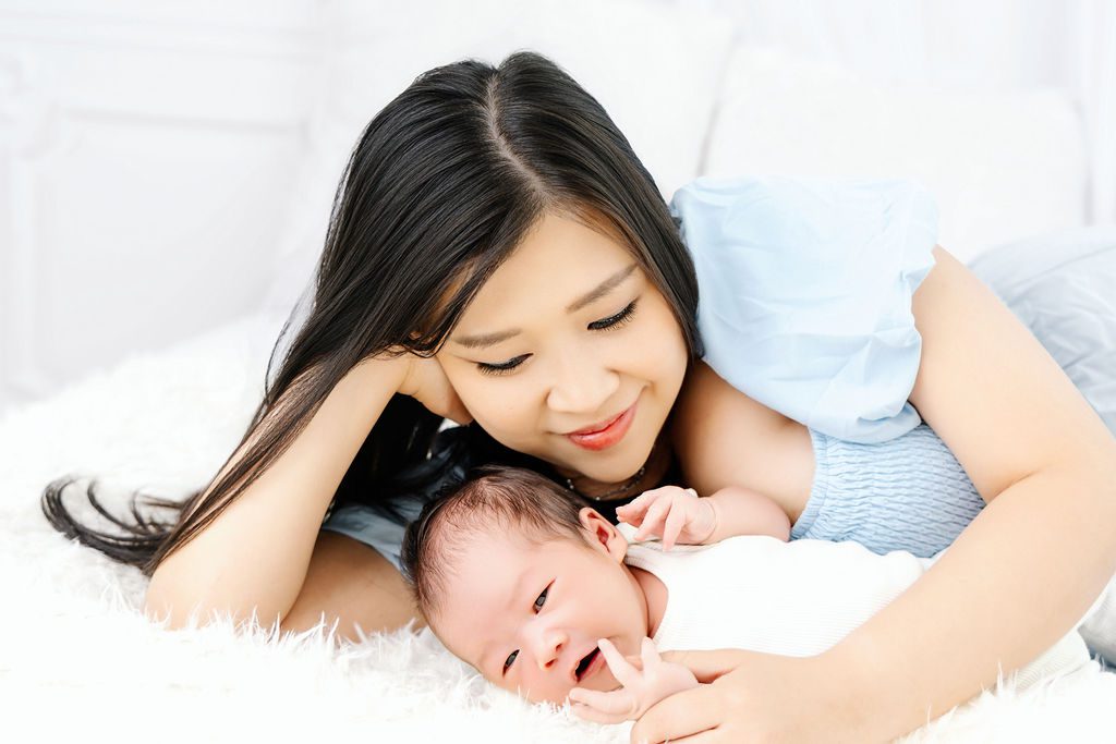 A happy new mom in a blue dress snuggles her awake newborn on a bed thanks to obgyns in austin