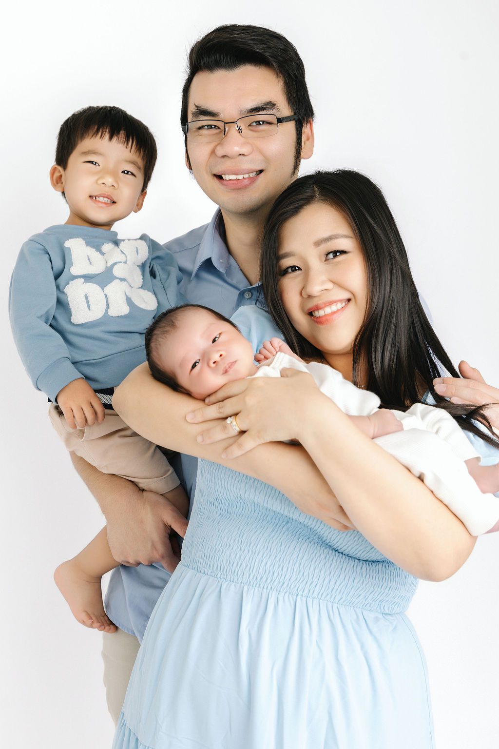 A happy mom and dad smile big while in blue with their toddler and newborn in their arms thanks to obgyns in austin