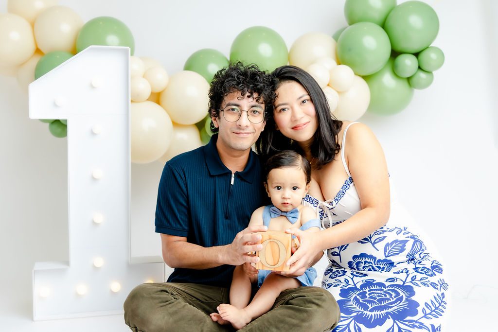 Happy mom and dad sit on the floor of a studio with their toddler in their lap in blue