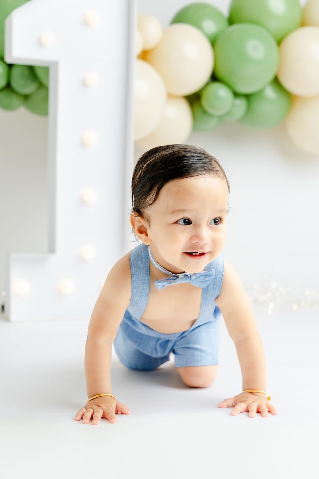 A baby in blue overalls and bowtie crawls on the floor of a studio after finding pediatric dentists in austin