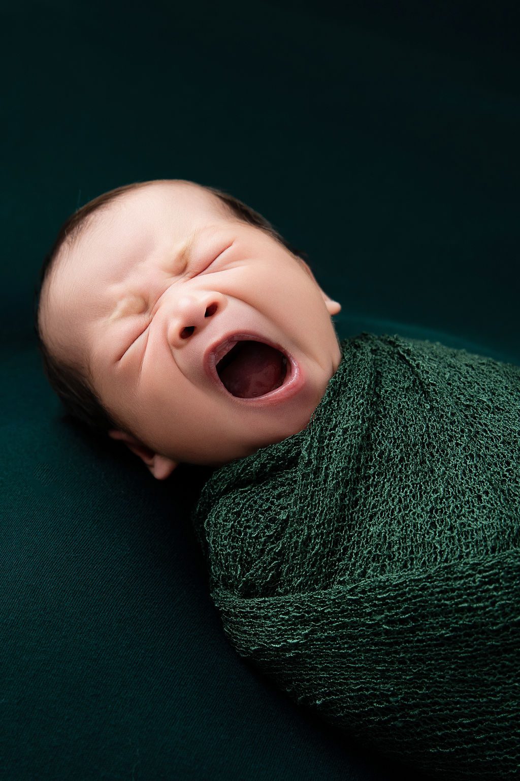 A sleeping newborn baby yawns while in a knit forest green swaddle