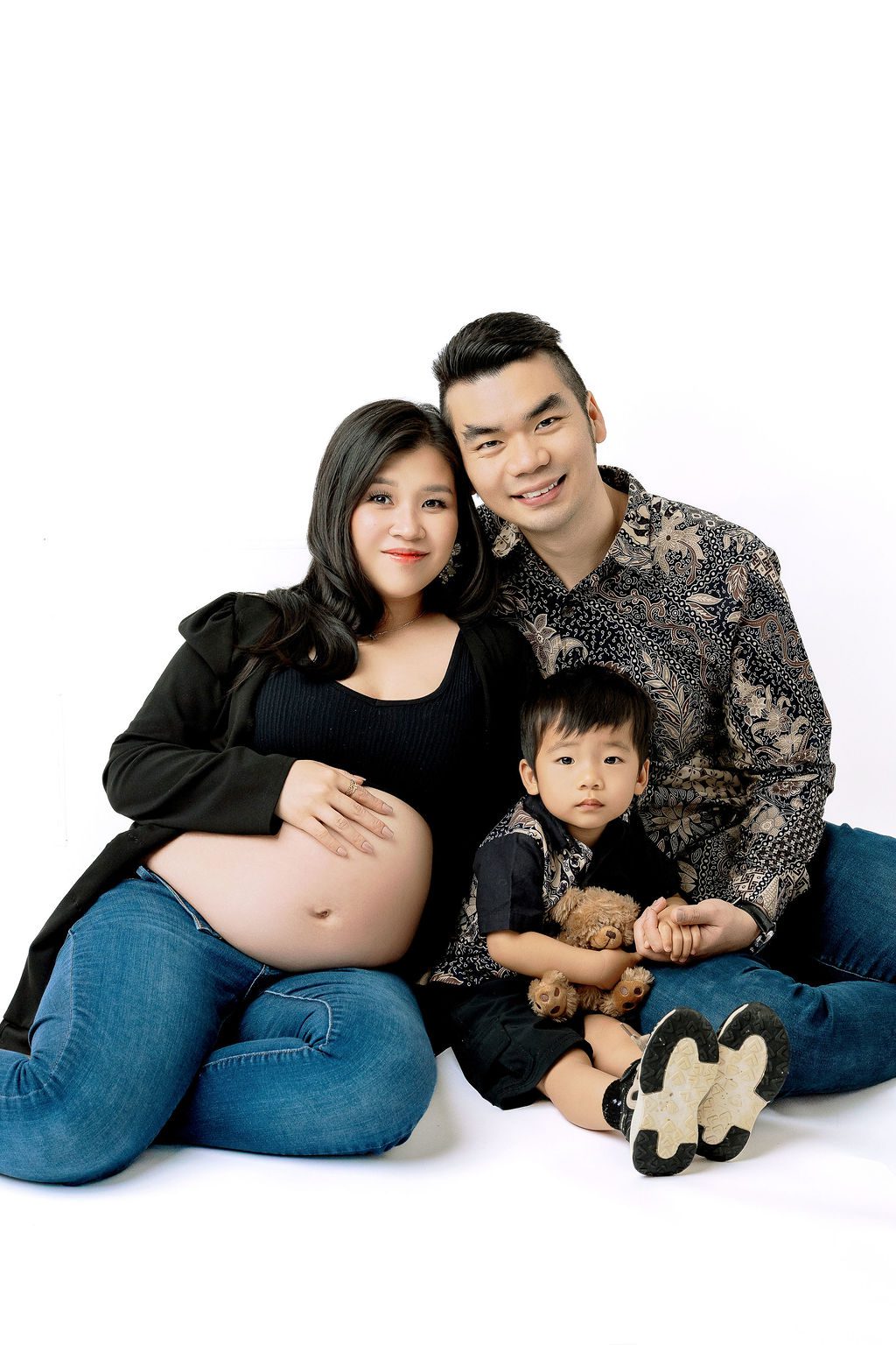 A smiling pregnant couple with the bump out sit on the floor snuggling with their toddler son between them thanks to fertility clinics in austin